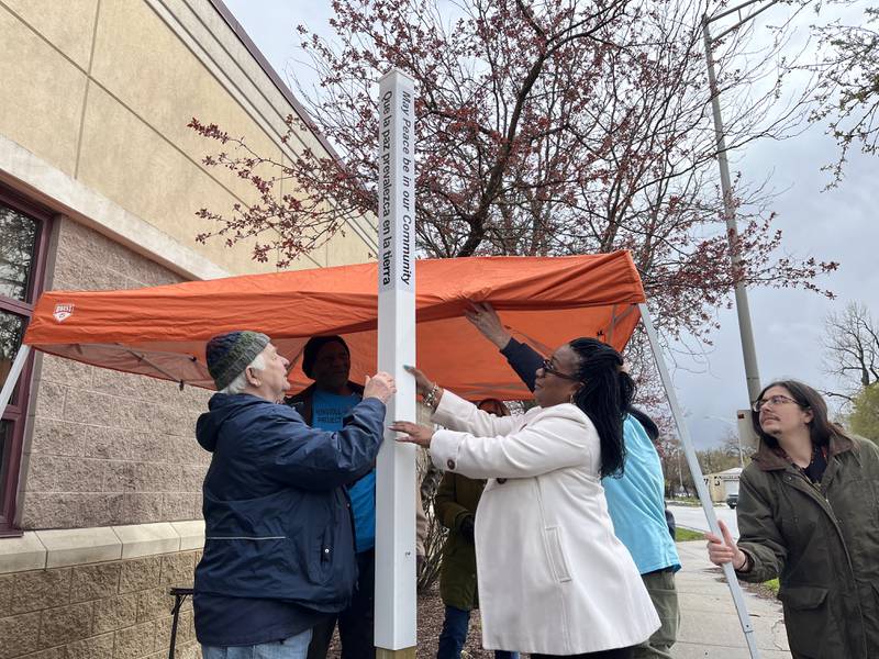 A peace pole is planted on Thursday, April 4 by Doug Kasper, chairman of Non-Violent Cities Project – Joliet (left), Nicole Lurry, community engagement coordinator for Peace Over Violence, and several others, outside the Ozzie and Peggy Mitchell Center in Joliet.