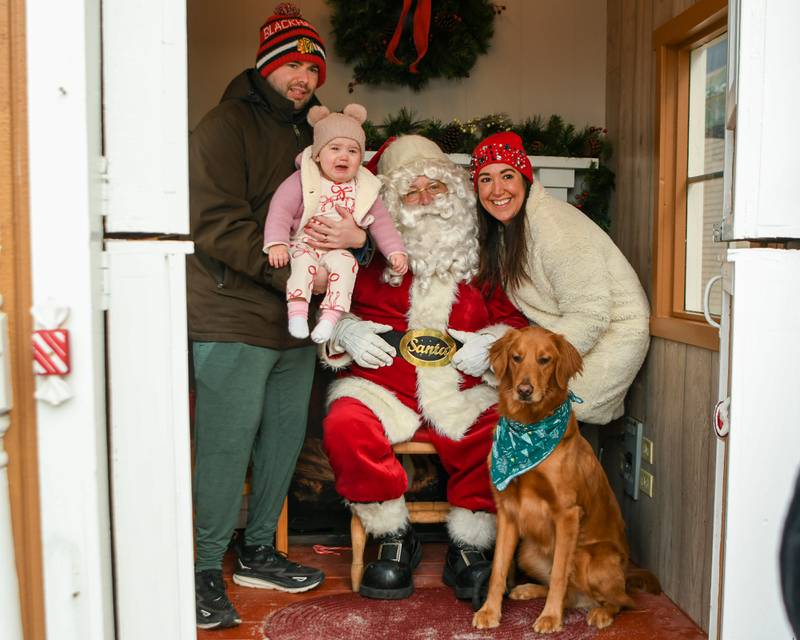 Brian Forhan holds his daughter Autum, 1, along with Lauran Forhan and their 2-year-old golden retriever name Dude pose for a photo as they visit Santa in his Gingerbread house on Saturday Dec. 21, 2024, in downtown Downers Grove.