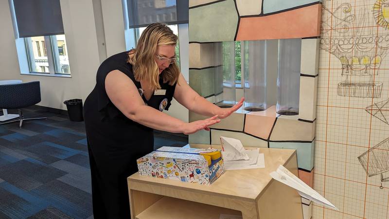 Mallory Hewlett, communications manager at the Joliet Public Library, demonstrates how to make and launch a paper airplane on Wednesday, June 21, 2023, at the Ottawa Street branch of the Joliet Public Library. The paper airplane launch is part of the “The Questioneers: Read. Question. Think. PLAY!” exhibit based on the Questioneers book series authored by Andrea Beaty and illustrated by David Roberts. The traveling, interactive exhibit is available during library hours through July 29.