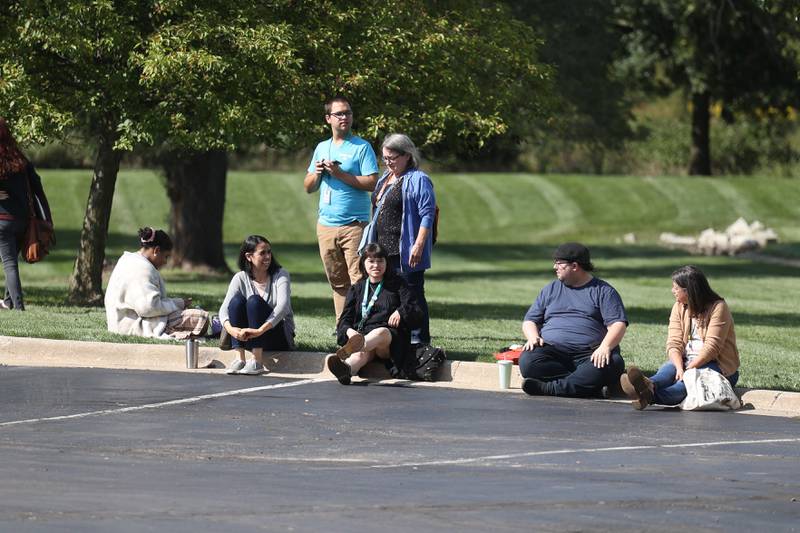 Staff of the Black Road Branch Library sit outside as police check the building after a bomb threat at that location on Thursday, Sept. 14, in Joliet.
