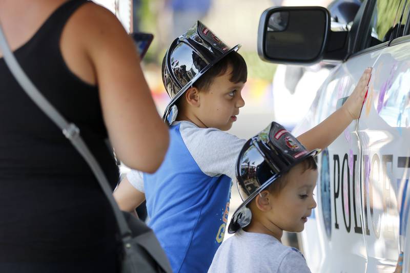Grace Mierwa, of Algonquin, left, takes a photo as her sons, Carter Serrano, 6, back, and Michael Serrano, 3, decorate an Algonquin police vehicle with painted handprints during a National Night Out event behind the Algonquin Area Public Library on Tuesday, Aug. 3, 2021, in Algonquin.  The nationwide event brings law enforcement personnel and the community together.