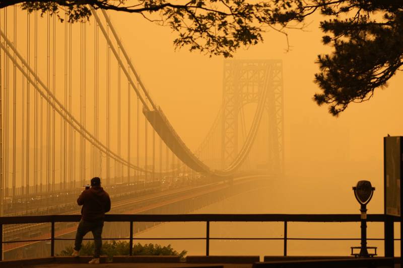 A Man talks on his phone as he looks through the haze at the George Washington Bridge from Fort Lee, N.J., Wednesday, June 7, 2023. Intense Canadian wildfires are blanketing the northeastern U.S. in a dystopian haze, turning the air acrid, the sky yellowish gray and prompting warnings for vulnerable populations to stay inside. (AP Photo/Seth Wenig)