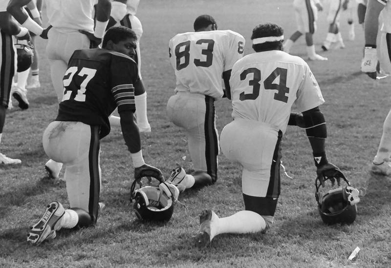Chicago Bears players Mike Richardson, Willie Gault and Walter Payton take a knee during training camp on Wednesday, June 12, 1985 in Platteville Wis.