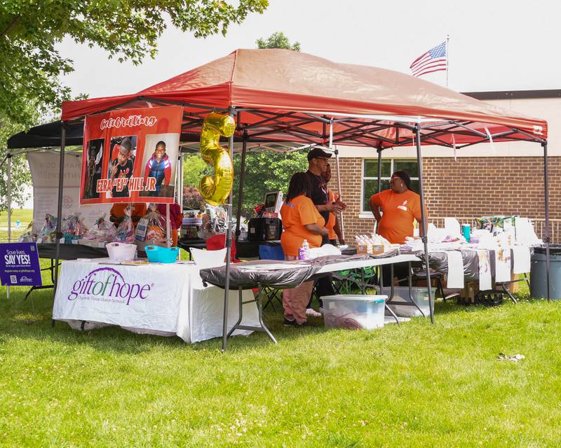 A group of tents are set up with raffle baskets, Gift of Hope Organ & Tissue Donor Network, and T-shirts to support the Ezra Hill Jr. Memorial Foundation on Saturday, June 7, 2025, for the foundation's 5th annual rock painting event held at Tyler Elementary School in DeKalb. The foundation was created to memorialize the late DeKalb boy, shot and killed in 2019.