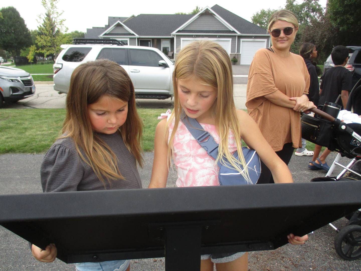 Lauren Roscoe watches as daughters Avery Roscoe, 7, and Vivian Callaghan, 8, students at Bristol Bay Elementary School, read one of the panels along the Yorkville Storywalk on Sept. 20.