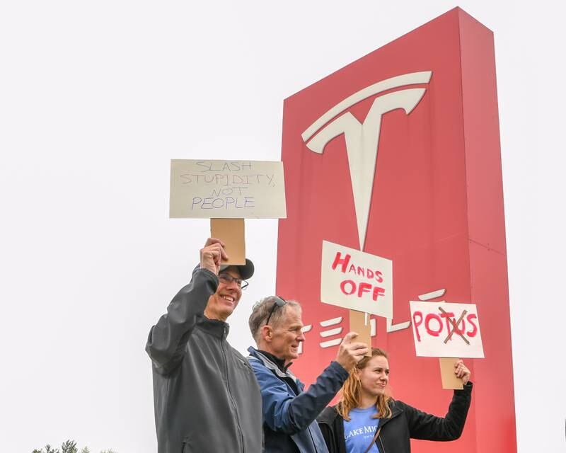Tom, Kevin and Abby all of Naperville hold signs outside the Tesla dealership on April 5, 2025, during the Hands Off Demonstration held along Ogden Ave. in Lisle.