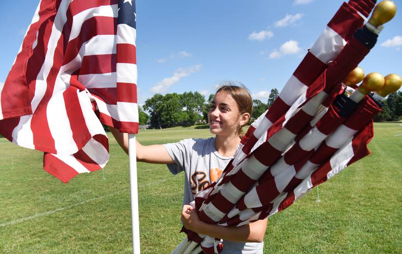 Grace Sirmon, 14, of Wheaton unwraps a flag during setup for the Wheaton Field of Honor at Seven Gables Park on Saturday, June 28, 2025.