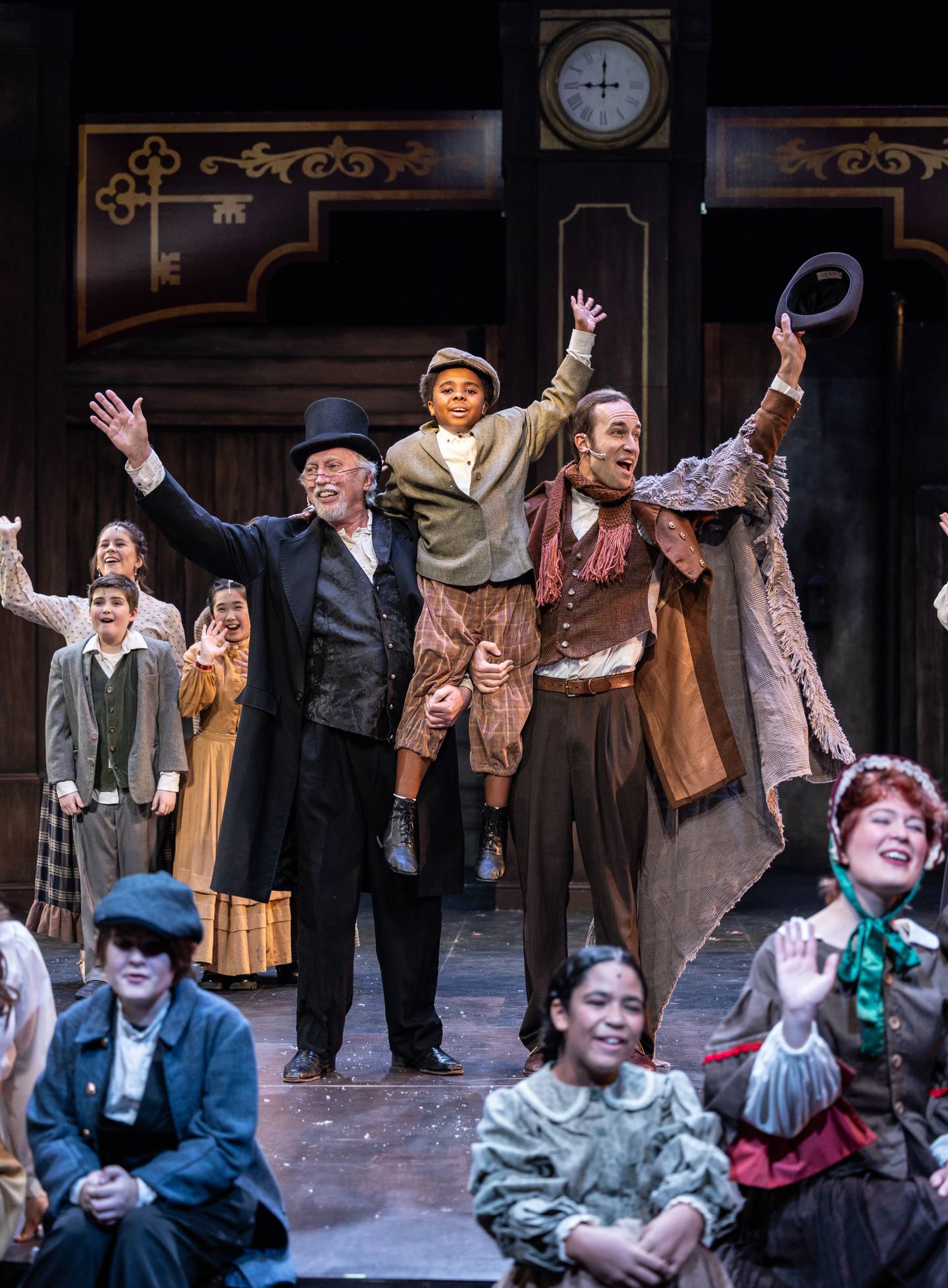 Scrooge (Stephen Connell of Crystal Lake, center left) and Bob Cratchit (Gabriel Fries, center right) hold up Tiny Tim (Christian Lucas) in "A Christmas Carol" at the Metropolis Performing Arts Centre in Arlington Heights through Dec. 23, 2024.