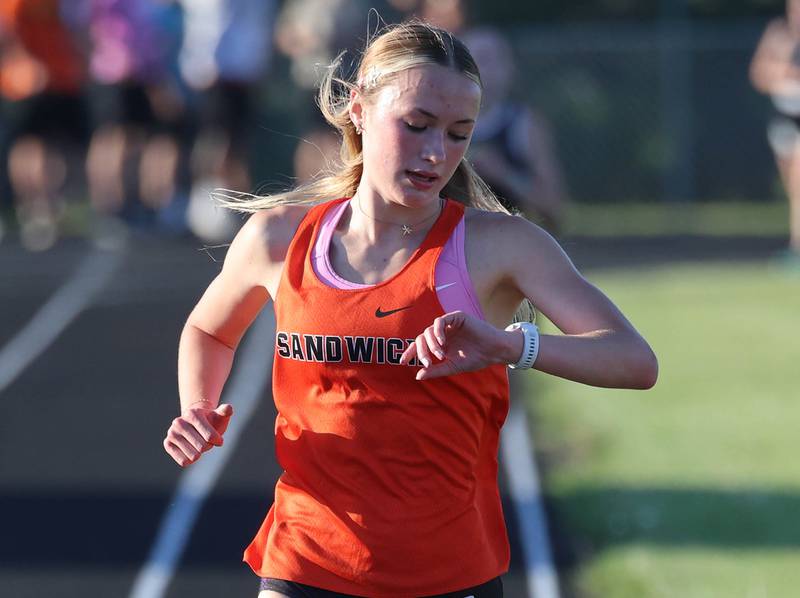 Sandwich’s Sundara Weber checks her time as she completes a lap in the 3200 meter run Friday, May 15, 2026, during the Class 2A girls track sectional at Genoa-Kingston High School.
