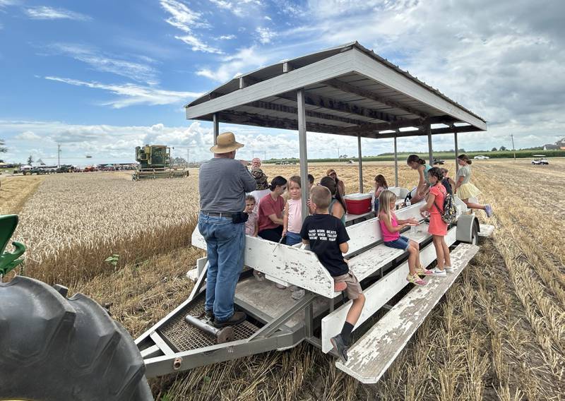 Roger Mixer of East Moline, shows kids how wheat is gleaned as a combine harvests a field in the background during a tour at the Bos Brothers Historical Farm south of Erie on Friday, July 25, 2025.