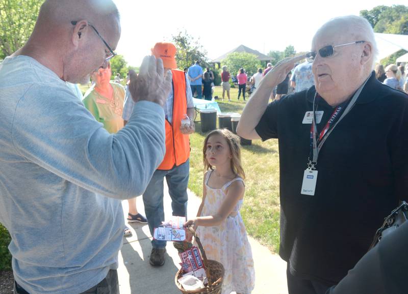 Serenity Home & Hospice Chaplain Willie Little (right) salutes Navy veteran Steve Rendleman, of Dixon, as Ahniya Wheeler, 6, of Mt Morris, hands him a "Thank You" card given at the memorial butterfly release on Saturday, July 8, 2023, in Oregon. Ahniya is the daughter of a hospice volunteer.