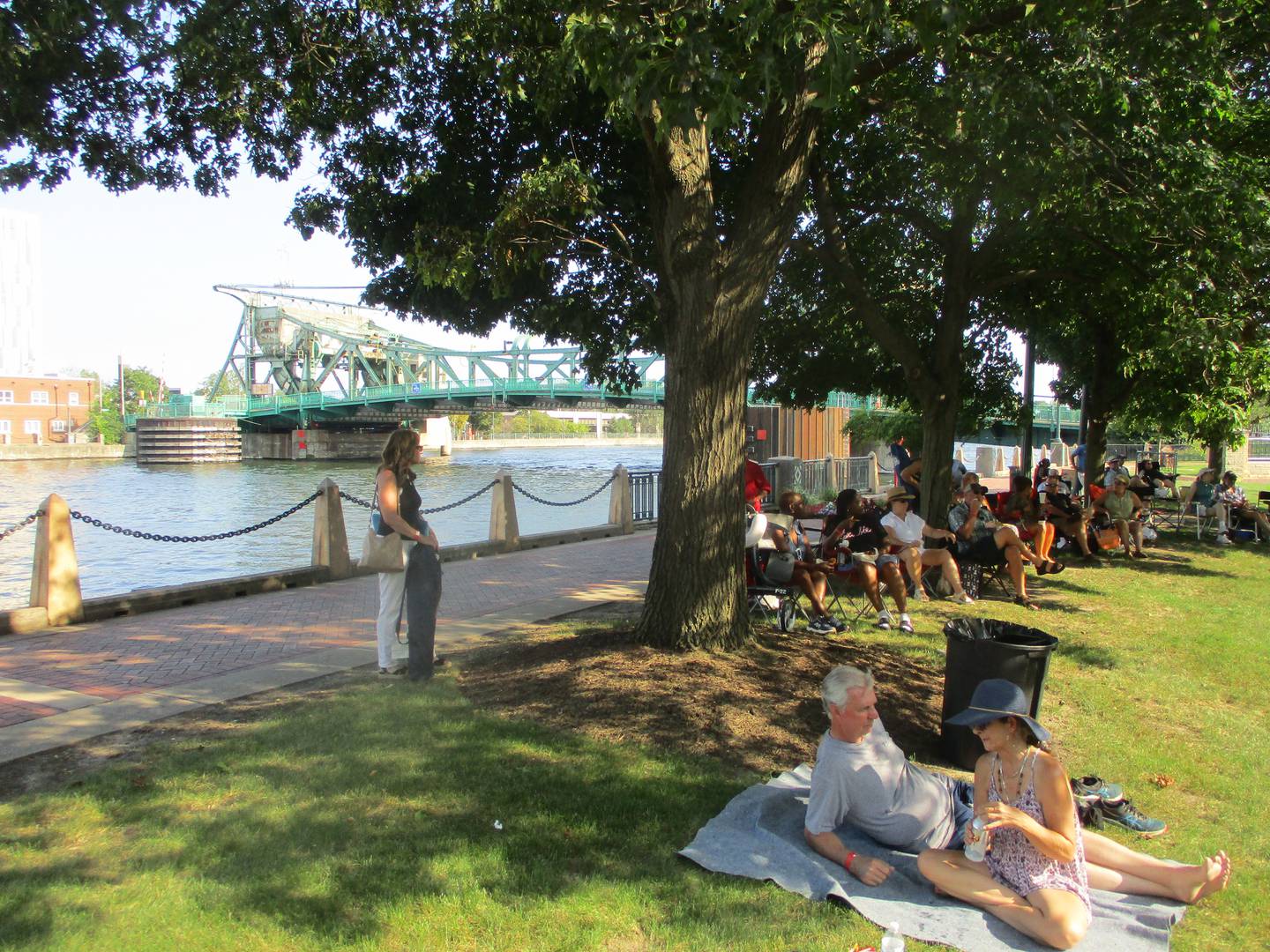 People at the Joliet Blues Festival take advantage of the shade provided by trees along the Des Plaines River at Billie Limacher Bicentennial Park amid 90-plus degree heat on Saturday. Aug. 9, 2025