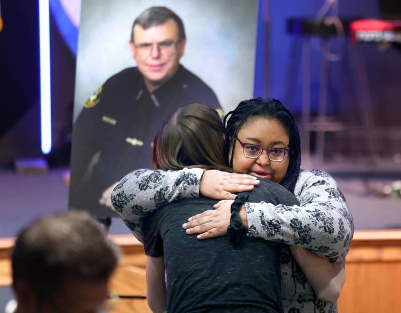 Members of the family of DeKalb County Sheriff Roger Scott, embrace in front of a picture of Scott during the memorial service for the former sheriff Friday, March 7, 2025, at Bethany Road Bible Church in DeKalb. Scott, who was the county sheriff for 36 years, died on February 23 at the age of 78.