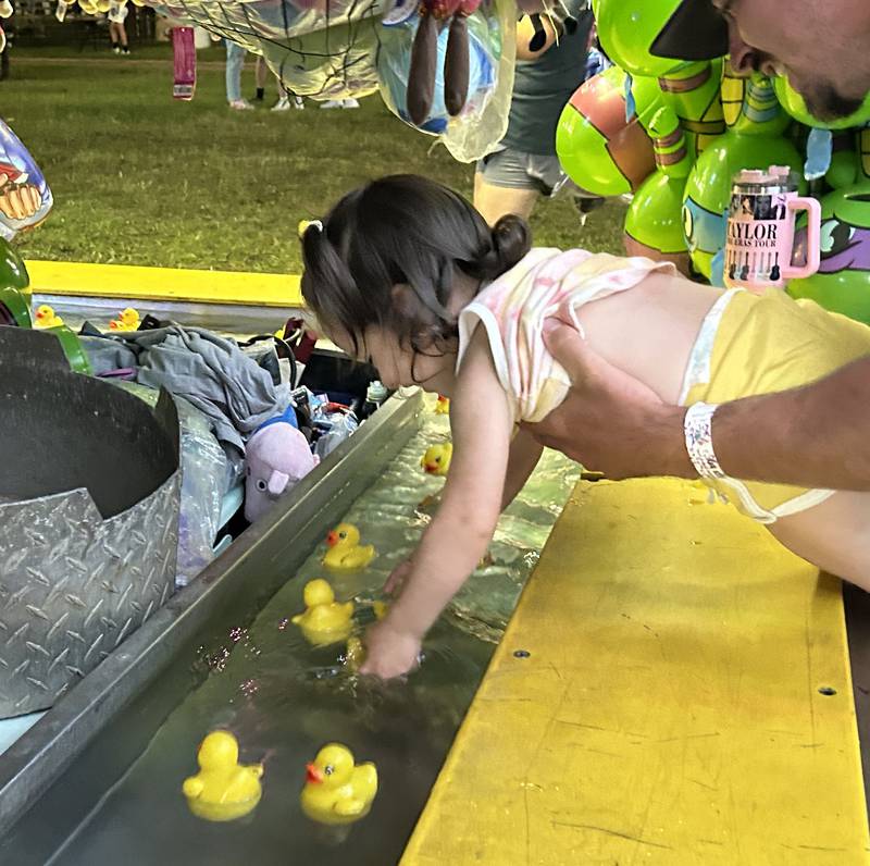Saylor Randecker, 2, of Lanark, gets some help to grab a plastic duck at one of the carnival midway games at the Ogle County Fair on Thursday, Aug. 1, 2024.