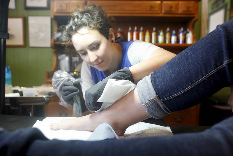 Em Becker of DeKalb Tattoo tattoos a pumpkin on the right foot of Jaqueline Wanket of DeKalb.