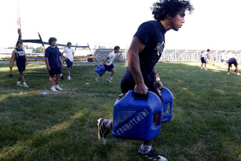 Cary-Grove’s Mykal Kanellakis runs with a weighted gas cans while doing conditioning drills during summer football practice Thursday, June 30, 2022, at Cary-Grove High School in Cary.