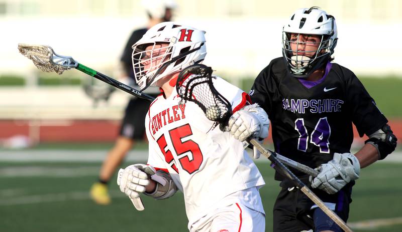 Huntley’s Andrew Baumley, left, gets past Hampshire’s Richard Henson in varsity lacrosse at Huntley Thursday night.
