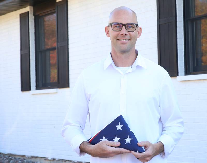 Veteran Cody Burroughs poses with an American flag outside his office on Monday, Oct. 31, 2023 in Spring Valley.