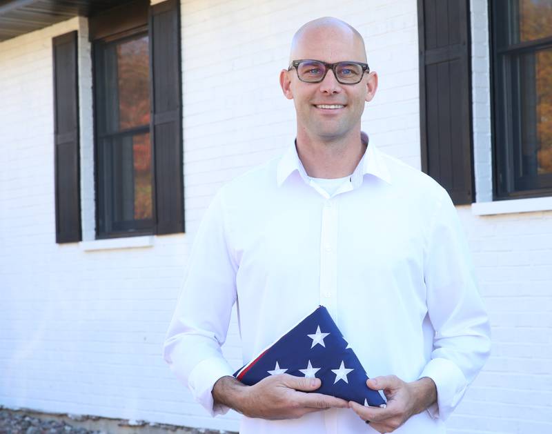 Veteran Cody Burroughs poses with an American flag outside his office on Monday, Oct. 31, 2023 in Spring Valley.