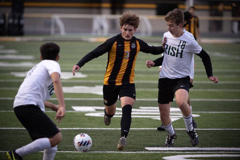 Herscher's Jacob Benoit, center, moves the ball forward as Bishop McNamara's Aiden Belcher, right, defends in a regional match-up on Tuesday, October 21, 2025.