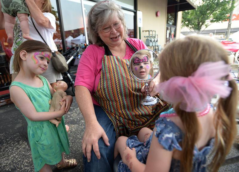 Riley Heiple of Berwyn supportively watches while her friend Parker Hopkins of LaGrange looks at the results of her face painting by Wina Shelley of Chicago during the annual LaGrange Craft Fair Saturday July 15, 2023.