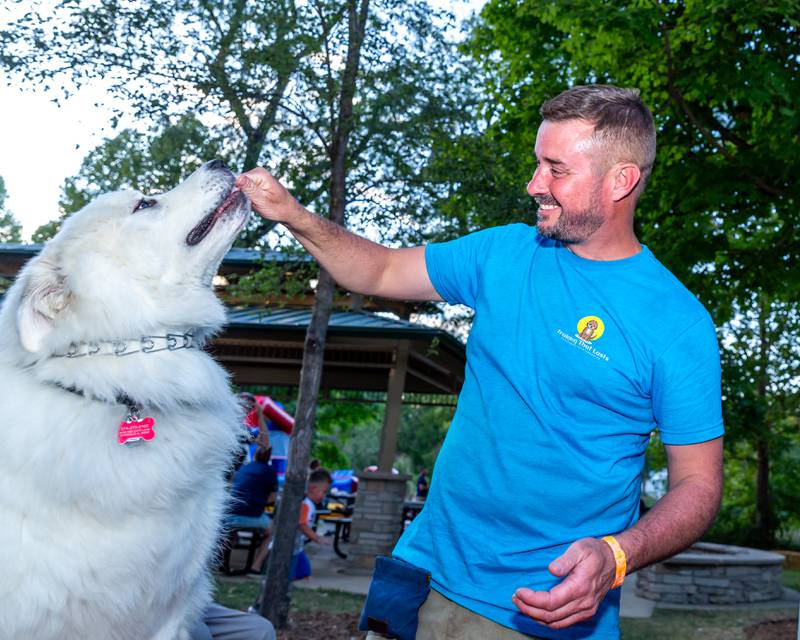 Tuyler Morrick, owner of Training that Lasts, feeds a treat to a large Samoyed at the Brew at the Bridge event. Sept 21, 2024 in Oswego.
