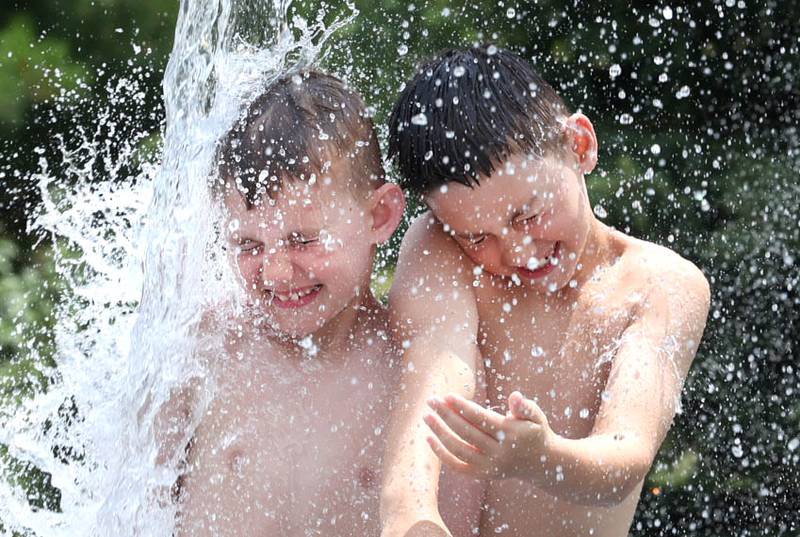 Rhett Hintzsche (left) and Bo Burdick, both 8, from Sycamore, get a bucket of water on their heads Thursday, June 20, 2024, at Splash Fountain Splashpad at the Sycamore Park District’s Legacy Campus on Airport Road. High temperatures have been over 90 degrees every day this week making splash pads and pools very popular destinations.