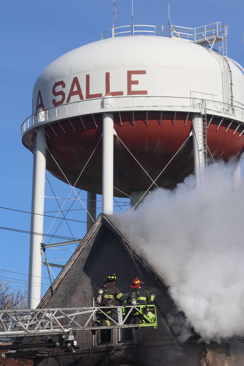 Firefighters position the Peru aerial ladder truck at the top of the attic of a buring structure fire as the La Salle water tower is visible overhead in the 800 block of Bucklin Street on Friday, Jan. 23, 2026 in La Salle.