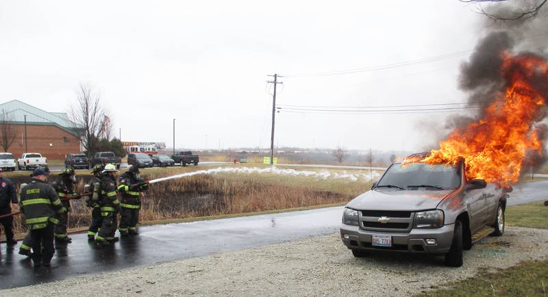Local elected officials from Oswego, Montgomery and Kendall County train a fire hose on a flaming car. They donned firefighter gear from the Oswego Fire Protection District for a training session at the district's Montgomery station. (Mark Foster -- mfoster@shawmedia.com)