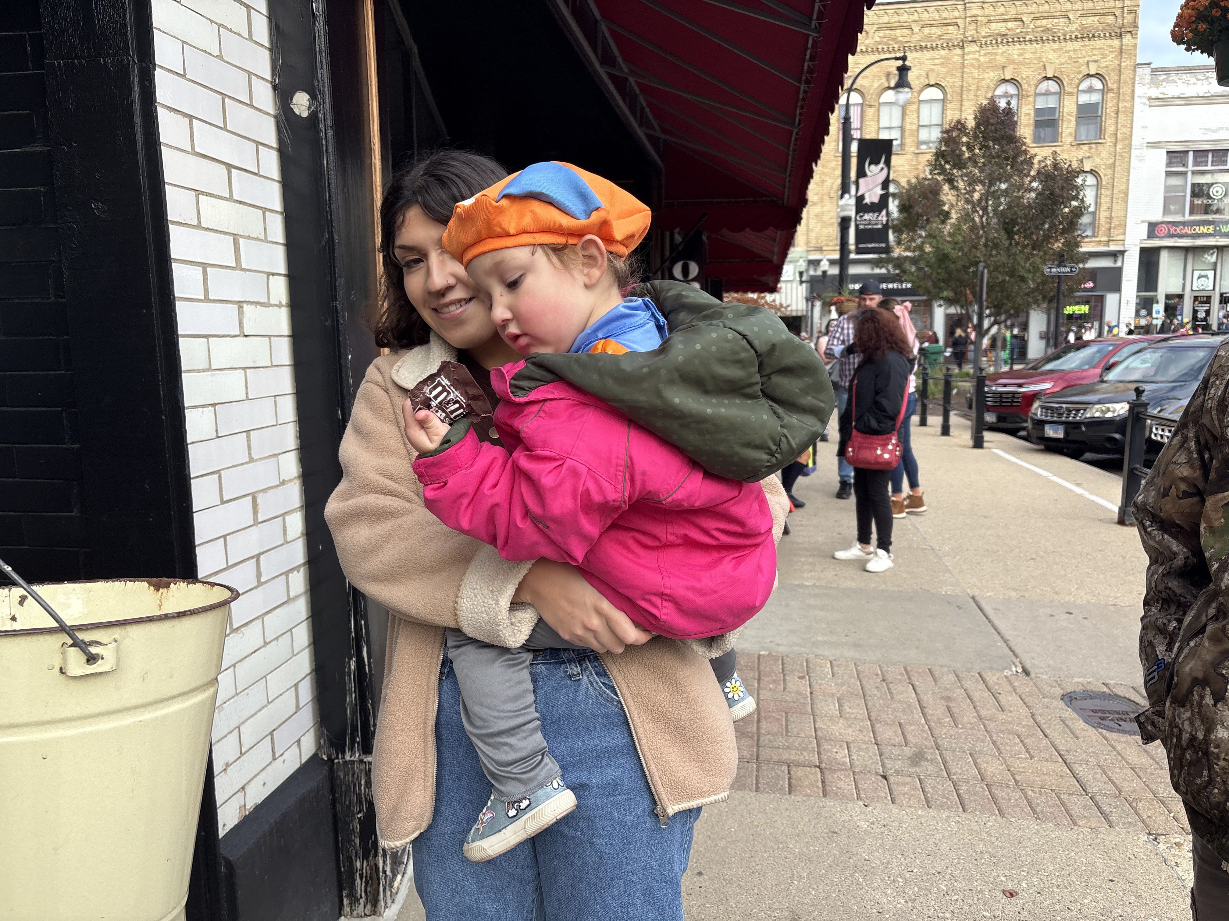 Lucia Navarro, 2, of Woodstock grabs a piece of candy and is held by her mother, Grecia Navarro, at The Backdrop during Halloween on the Square in Woodstock Oct. 31, 2025.