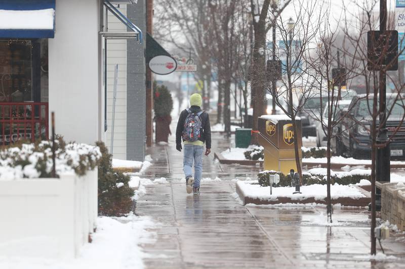A pedestrian walks the slushy sidewalk along Lockport Street in downtown Plainfield as morning snow turned to afternoon rain on Tuesday, Jan. 9th, 2024.