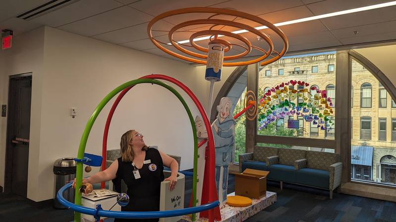 Mallory Hewlett, communications manager at the Joliet Public Library, shows how kids can "fly" with engineer Rosie Revere in her Cheese Copter on Wednesday, June 21, 2023. Rosie in one of the characters featured in “The Questioneers: Read. Question. Think. PLAY!” exhibit is based on the Questioneers book series authored by Andrea Beaty and illustrated by David Roberts. This traveling exhibit featuring the Questioneers characters opened June 16 at the Ottawa Street branch of the Joliet Public Library and is available during library hours through July 29.