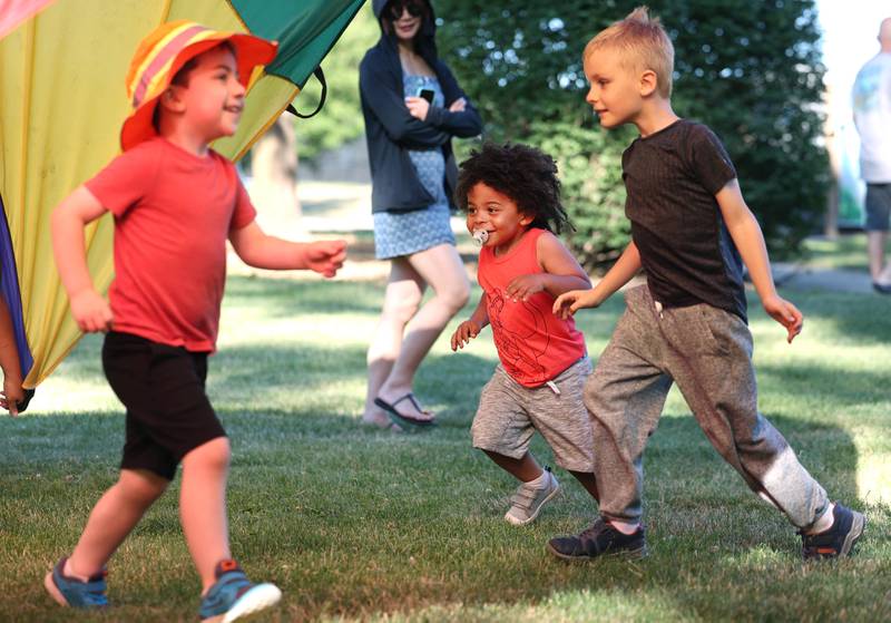Kids run under the parachute Friday, June 14, 2024, during a Dedication Celebration event at Hopkins Park for the grand opening of the new playground and racquet courts.