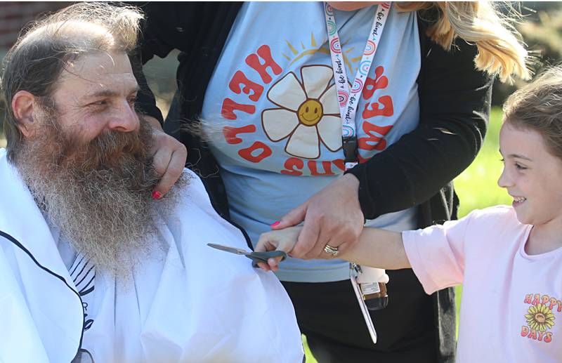 Custodian Bob Espel shaves his head with the help from Khloee during his head and beard shaving on Wednesday, May 22, 2024 at Douglas Elementary School in Princeton. Students raised more than $3.332 in the past few weeks. All proceeds will go to the new landscaping around the Douglas building, with the first round of plantings to take place with students present this Thursday, May 23. Using funds from the Preschool for All grant,the school has purchased new age-appropriate playground equipment to promote physical activity, creativity and social interaction.