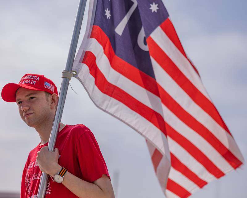 Leo Volker carries a flag to his vehicle during the caravan staging for the Trump Birthday and Flag Day Caravan and Rally on June 14, 2025 at Jamie's Outpost in Utica.
