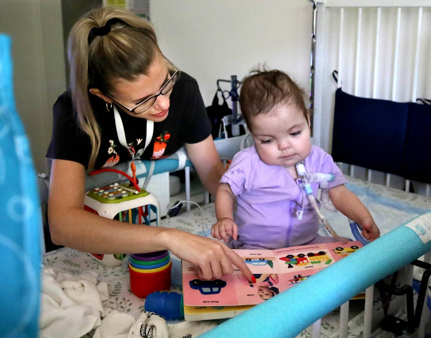 Marely Chavarria Santos, 1, looks at a book with home visitor Miranda Bates Monday, June 30, 2025, at Marely’s home in DeKalb. Marely was born with a myriad of health issues that require around-the-clock care and recently received a heart transplant.