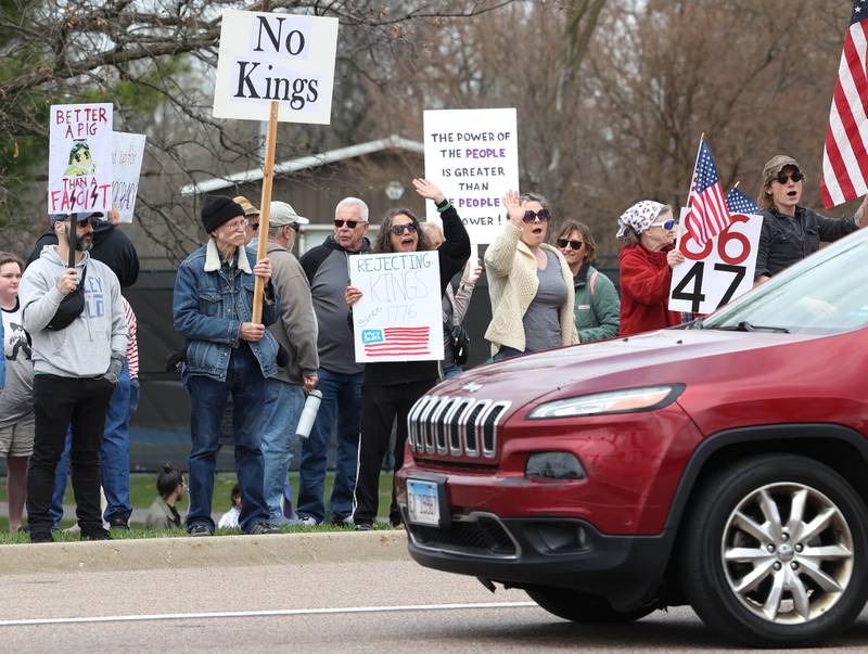 Protesters wave at passing vehicles along Sycamore Road in front of Hopkins Park Saturday, April 19, 2025, during a “No Kings” rally and march in DeKalb. The group was protesting what they’ve argued is the unlawful and harmful federal policies of President Donald Trump and his administration.