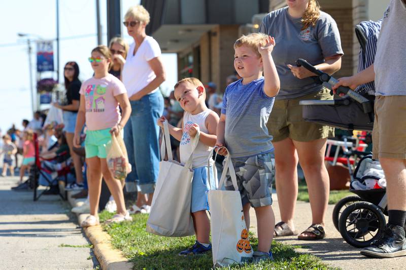 Two young paradegoers wave and await tossed candy at the Grand Pumpkin Parade during the St. Anne Pumpkin Festival on Saturday, Oct. 4, 2025.