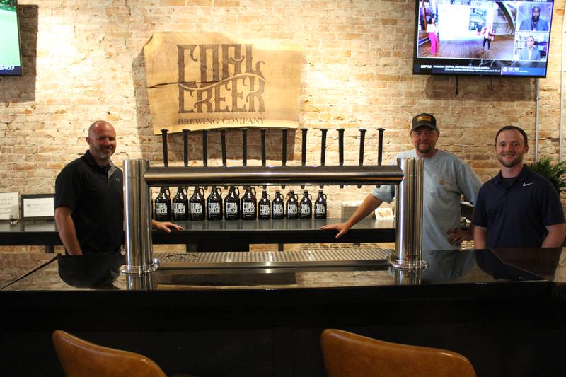 Michael Grieve (from left), Justin Stange, and Trevin Kennedy stand next to the impressive tap at Coal Creek Brewing Company in Princeton.