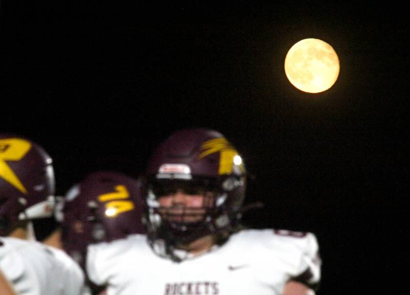 The moon rises as Richmond Burton’s Rockets warm up for varsity football at Rod Poppe Field on the campus of Marengo High School in Marengo on Friday, Oct. 18, 2024.