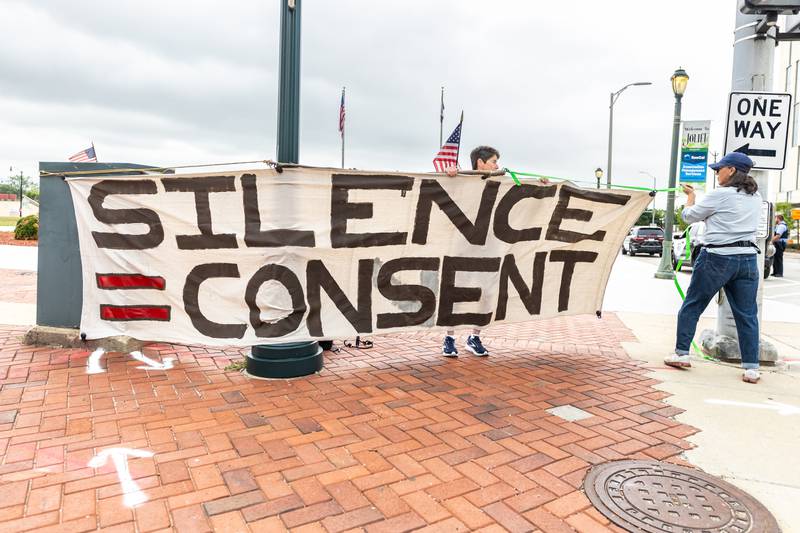 Attendees hang a big sign on Jefferson Street in Downtown Joliet during the Good Trouble Lives On event on July 17, 2025.