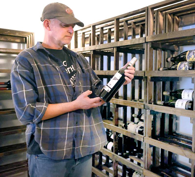 Thomas Sherman, owner of  Class VI Wine & Charcuterie, looks at one of the bottles of wine Friday, April 28, 2023, that will be available at the new restaurant located at 214 E. Lincoln Highway, in DeKalb. Sherman is a U.S. Army veteran.