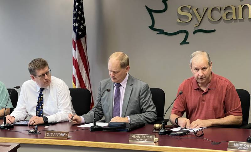 (From left) Sycamore City Manager Michael Hall, looks on as city attorney Kevin Buick crosses off an item on a sheet of paper while 1st Ward Alderperson Alan Bauer speaks during the Sept. 5 2023 Sycamore City Council meeting.