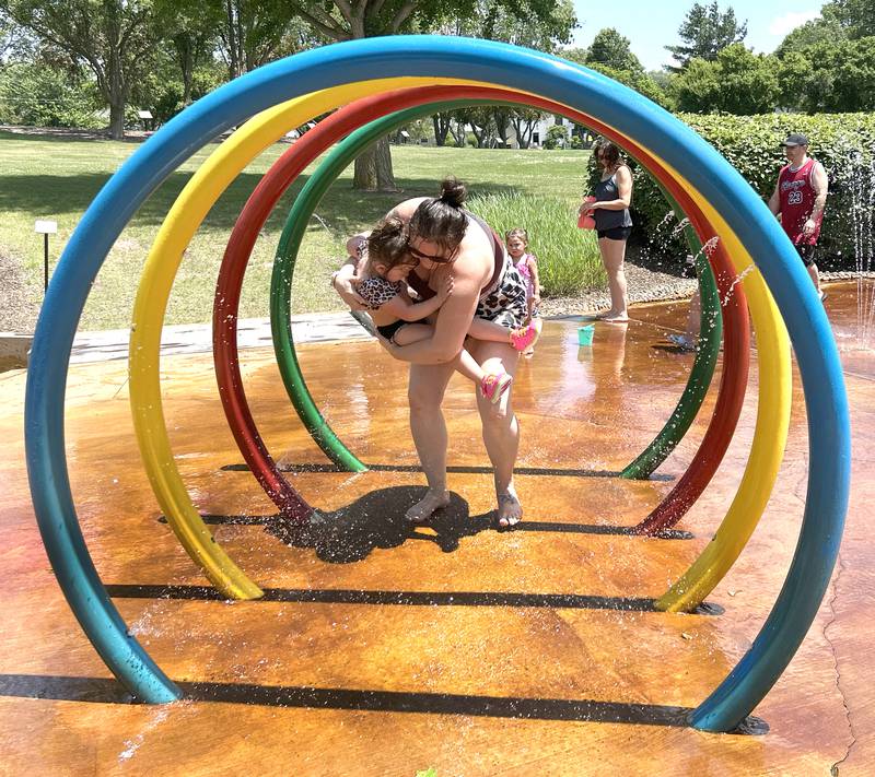 Elyn Gibson of Rockford carries her daughter Sylvia, through one of the water features at the Oregon Park District's splash pad on Sunday, June 22. The free water attraction is a popular hot-weather destination as temperatures reach the mid-90s