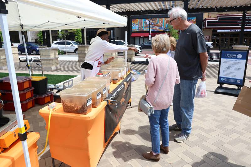 Customers line up at the Nuts to Go tent at the new city square for the farmers market on Friday, May 22, 2026 in Joliet.