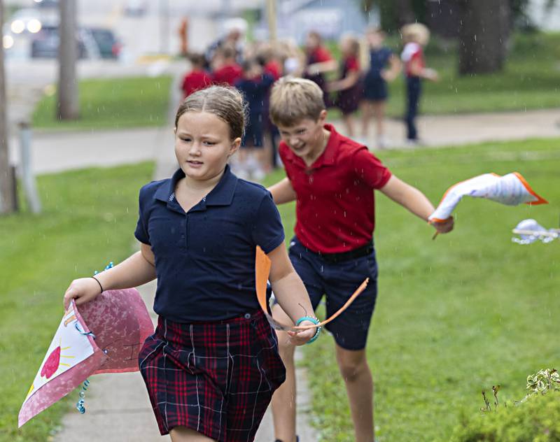 St. Mary’s students Avery Storey and James Catt scramble through the rain Friday, Sept. 22, 2023 after picking up signs made for the school’s annual “Walk, Pray, Love-a-Thon.” A drizzle cut some events short but the goodwill stayed all day.