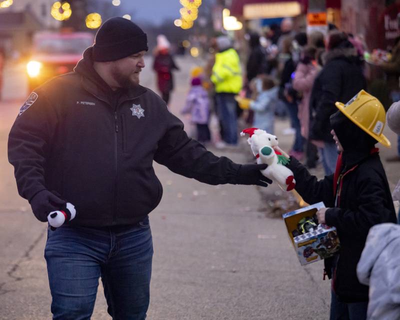 Oglesby policeman Paul Peterson hands out a stuffed animal and other toys to children along the Oglesby Winter Parade route on December 9, 2023.