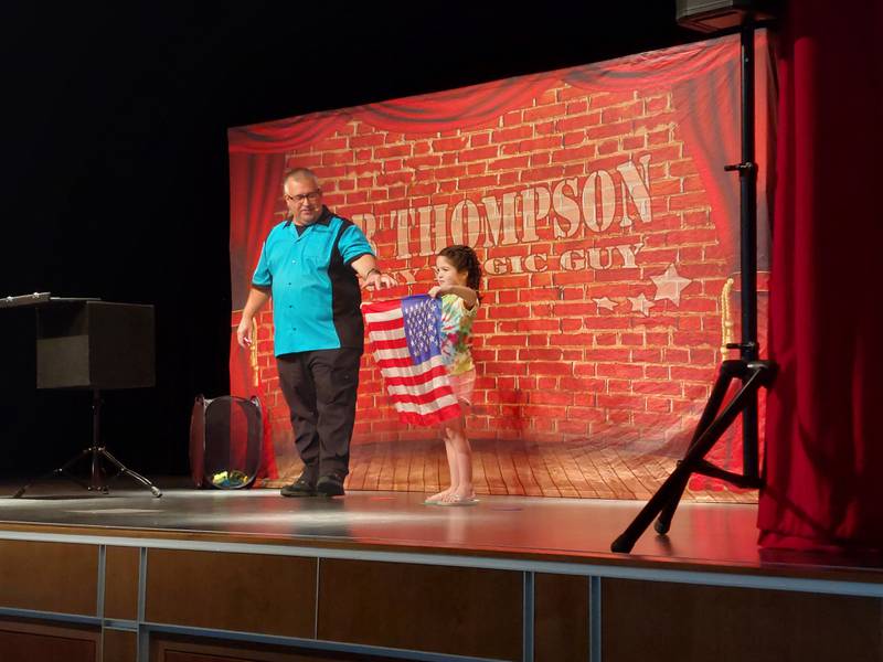 Nora holds up an American flag after magician Rob Thompson performs a trick turning handkerchiefs into the flag Wednesday, June 21, 2023, during a show sponsored by Ottawa Recreation at Central Intermediate School.