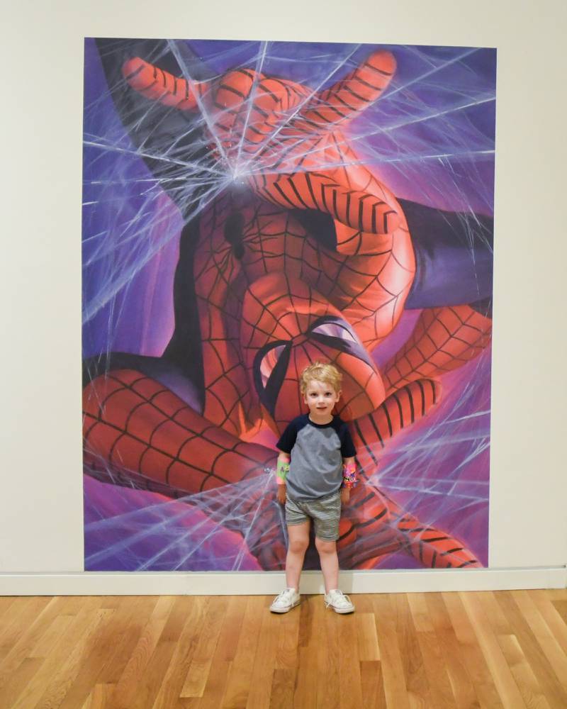 Cary Suex, 3 years old, of Downers Grove poses next to a spider man painting as part of The Marvelcity: The Art of Alex Ross exhibit held at the Elmhurst Museum on Saturday June 24, 2023.
