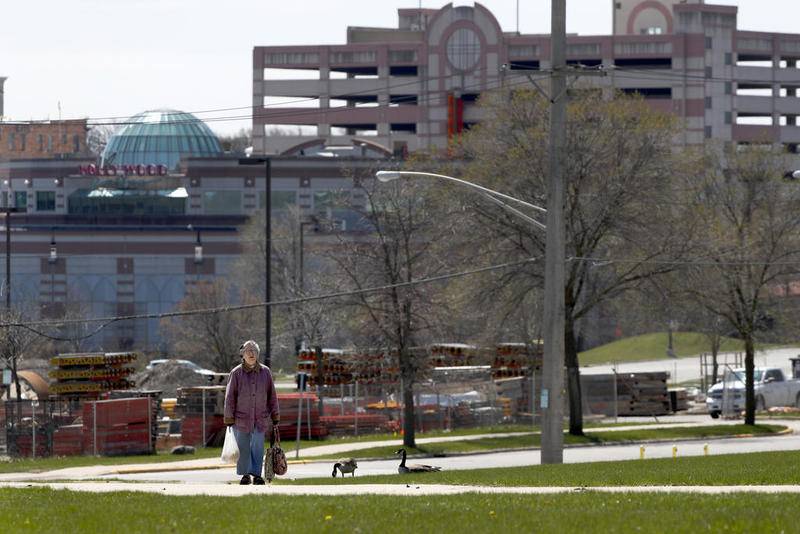 A lone elderly woman carries her grocery bags up a hill as the closed Hollywood Casino rises up behind her near downtown Aurora, Ill., Monday, April 20, 2020.